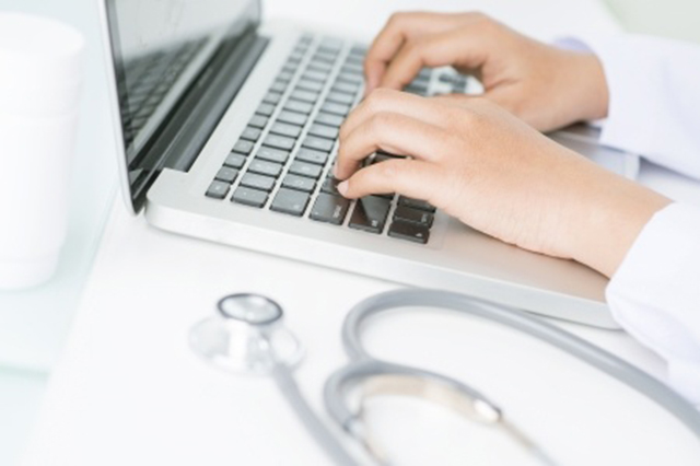 Image doctor using laptop. Shows close-up of keyboard, hands and stethescope in soft colours
